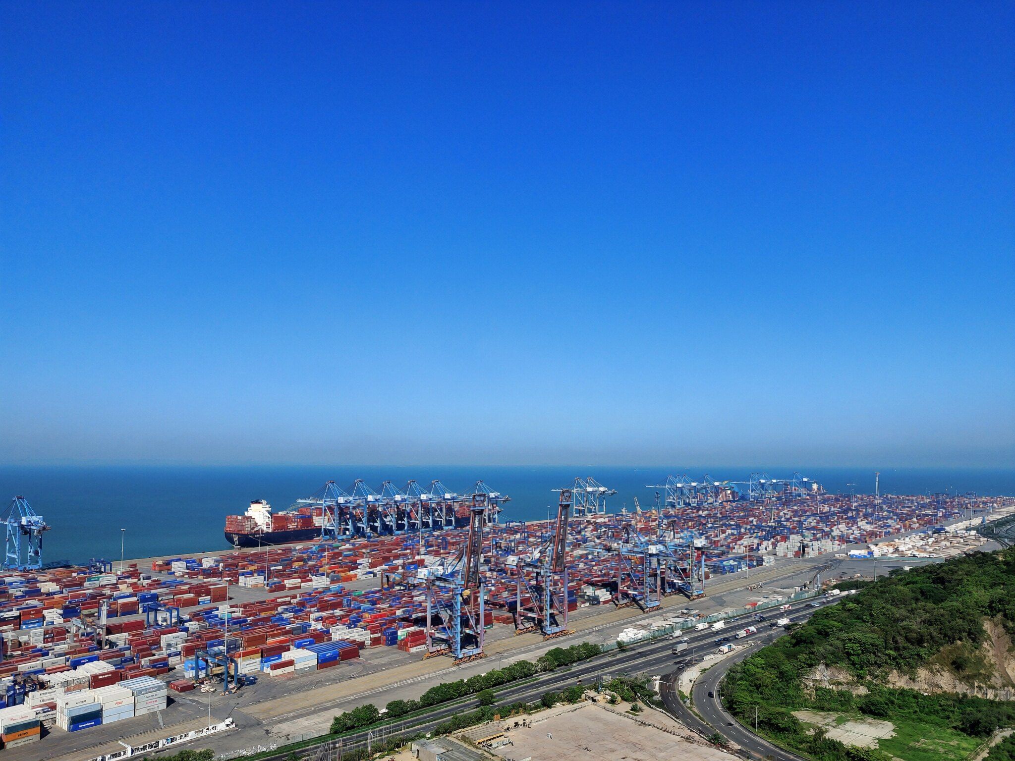 Porto de contêineres com guindastes e um navio atracado, visto do alto